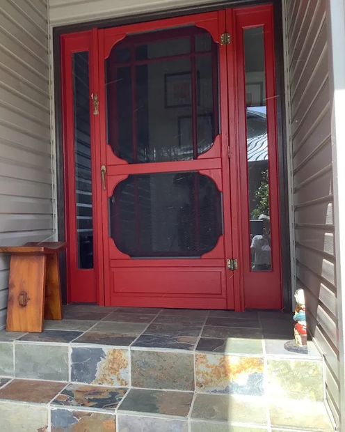 Red front screen door with glass panels at the top of tiled porch steps