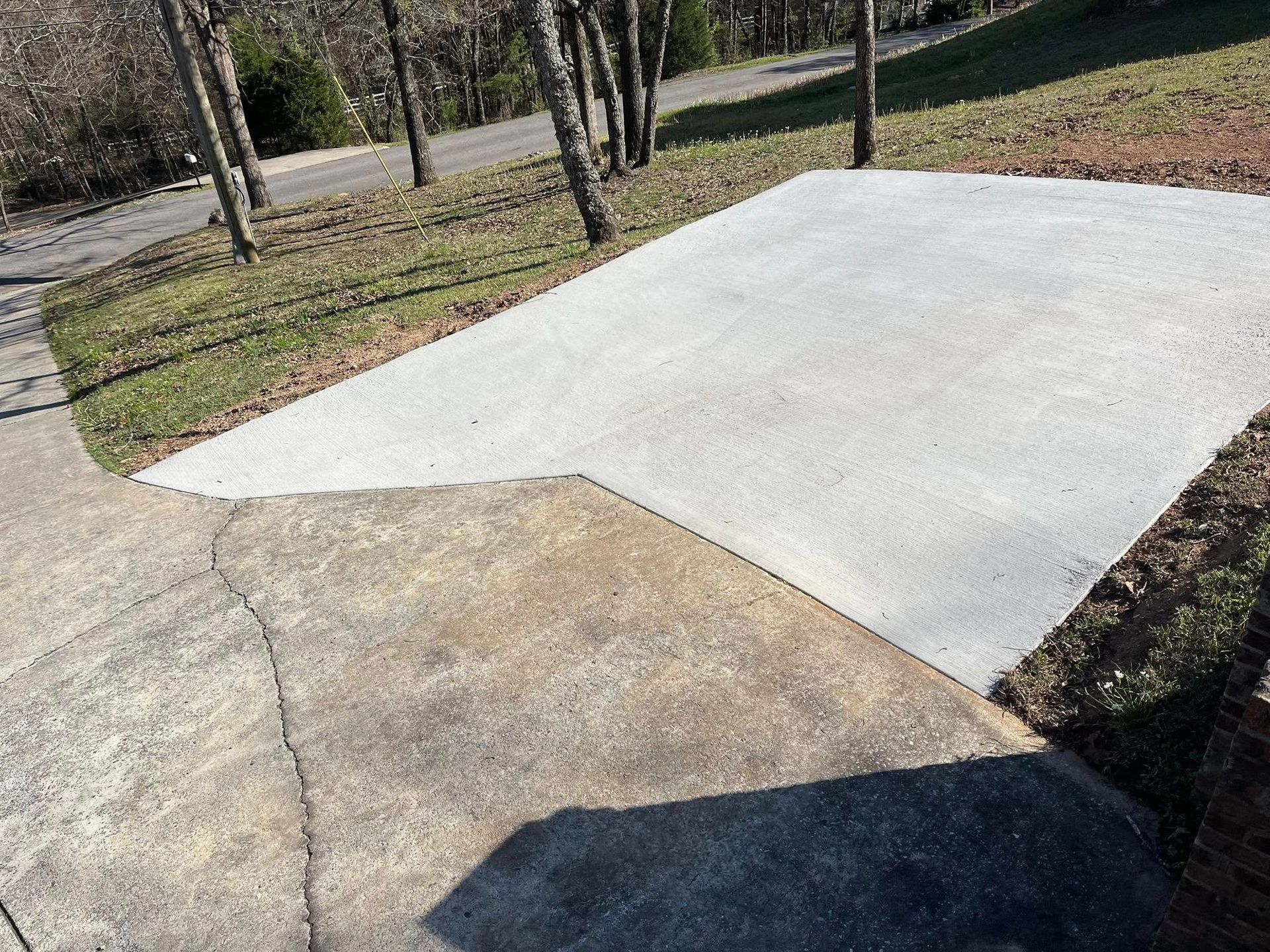 A newly poured, light-gray concrete pad extension connected to an older, weathered driveway in a residential yard.