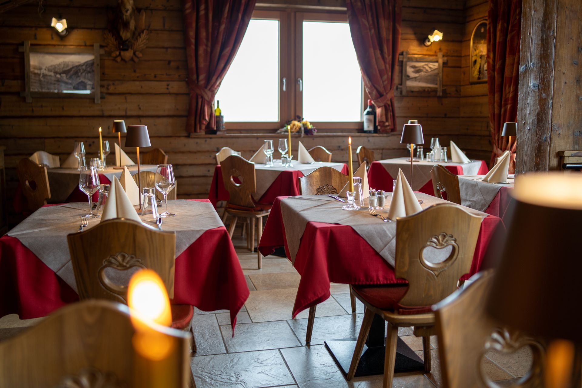 Interno di un ristorante con pareti in legno, tavoli apparecchiati con tovaglie rosse e una finestra con tende rosse.