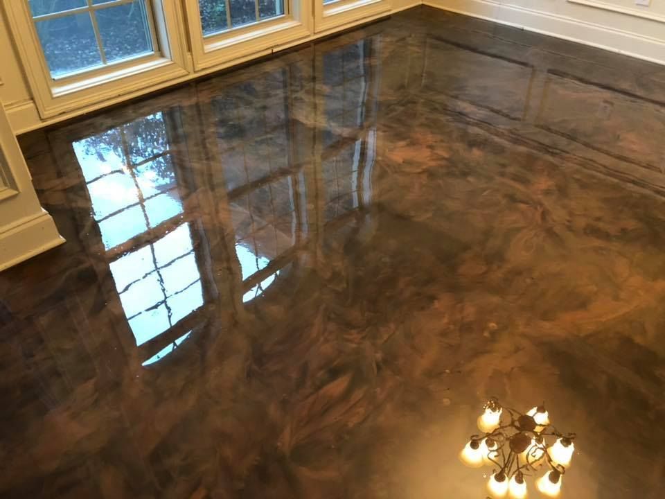 Metallic epoxy floor reflecting windows and a chandelier; brown and bronze tones.