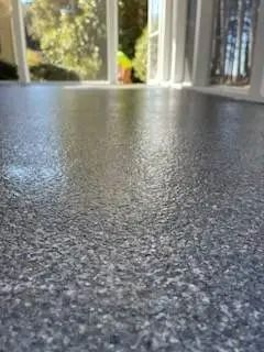 Close-up of a textured, speckled, gray floor reflecting sunlight from windows in a bright room.