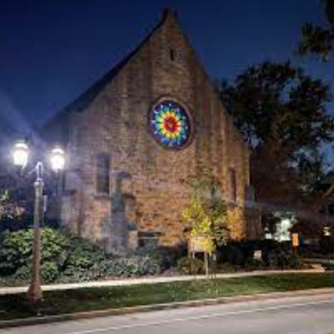 Brick church building at night with lights and the rose window lit up