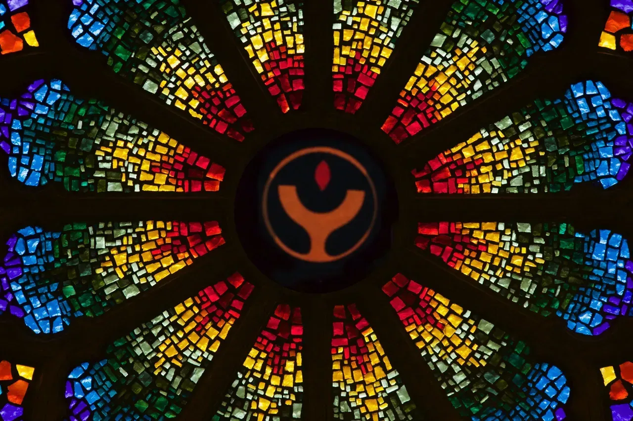 Rose Window with a stylized Chalice with a small flame in the center.