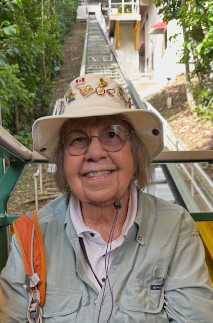 Older white woman with gray hair, large framed glasses and a cool hat with fun pins on it