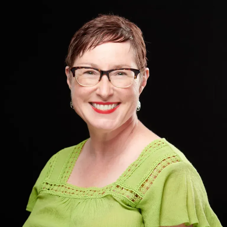 Middle aged white woman with short brown hair and oval bold framed glasses