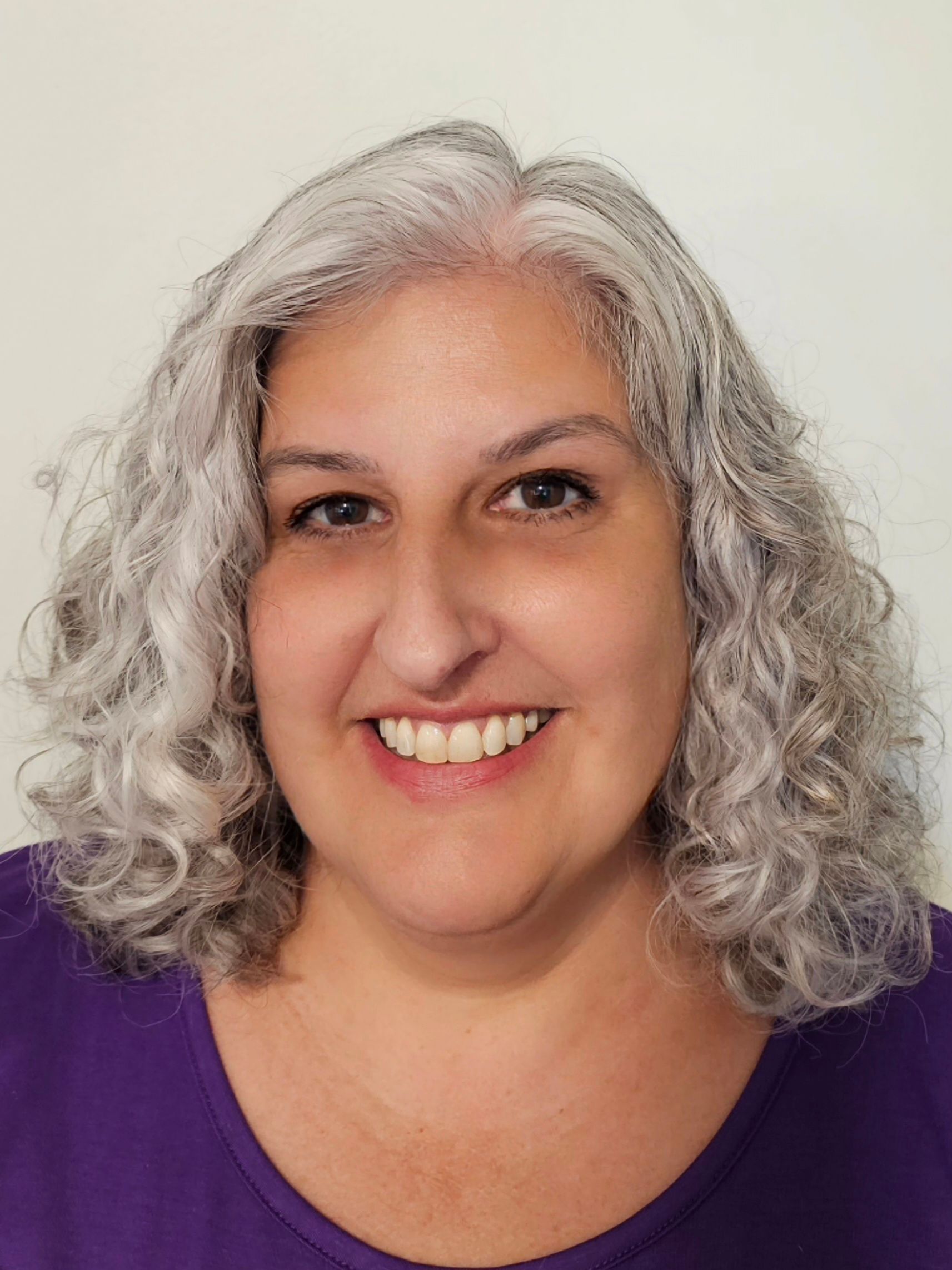 Middle aged white woman with gray curly short hair and a big smile