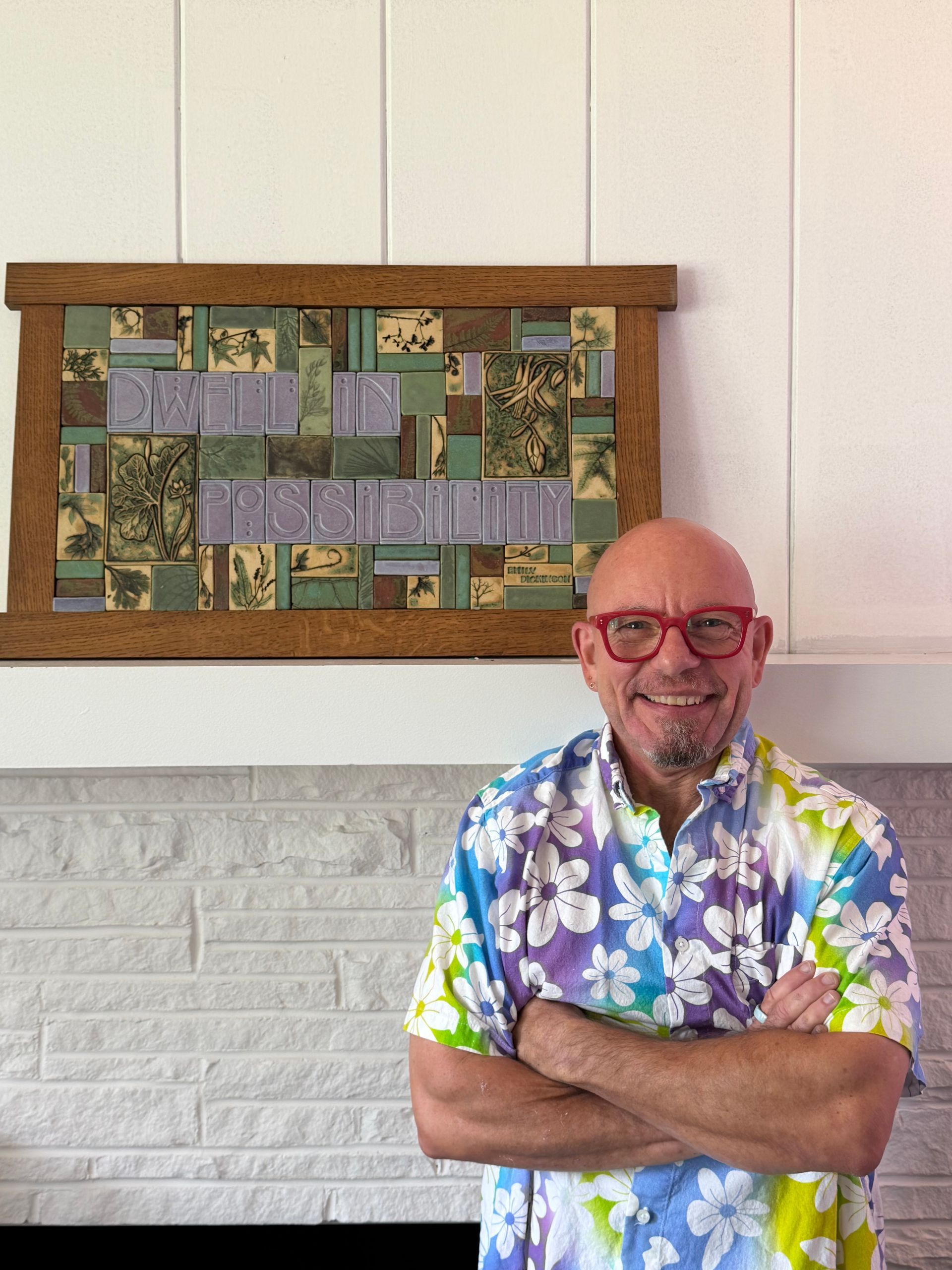 A bald white man with glasses smiling in front of some art
