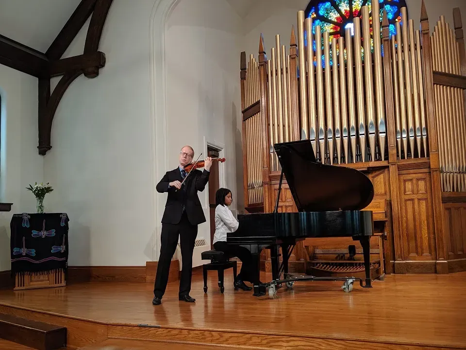 Man playing a violin on the Sanctuary stage with a woman playing the piano in front of them. They are in front of the organ.