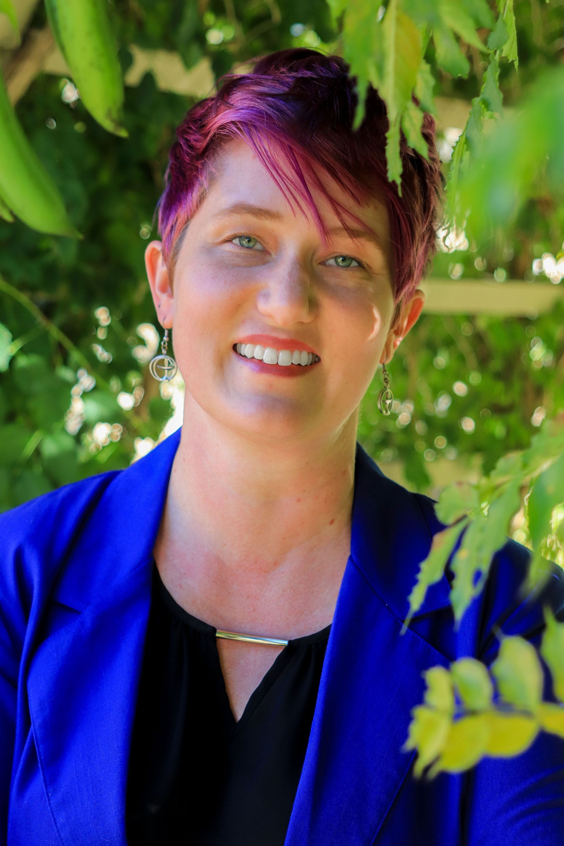 Rev. Sally Fritsche is a 30 something with purple short hair. She is smiling. She is wearing a light blue button down.