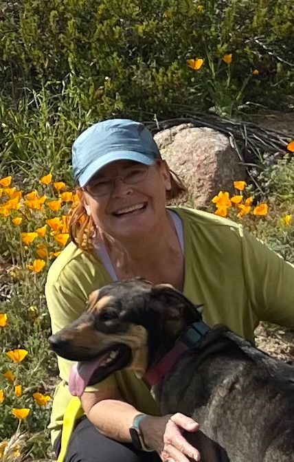 a white woman in a hat in nature with a brown dog