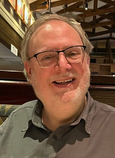 An older white man with glasses smiling at the camera