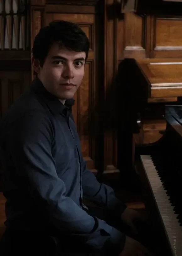 Hispanic man with dark hair sitting behind a piano