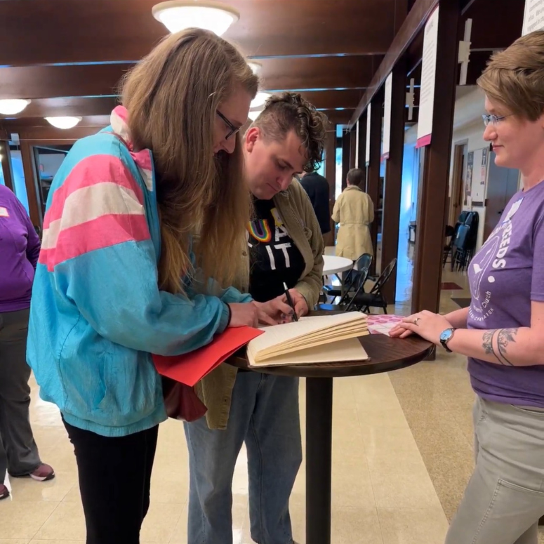 Two congregants are signing the membership book with Rev. Sally Fritsche looking on.