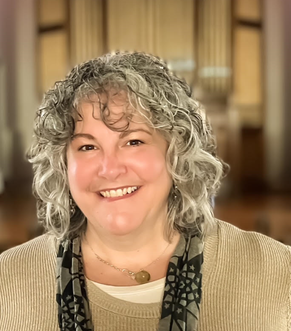 Kelly Skinner is a middle aged woman with curly black and white shoulder length hair. She has bangs and a smile.