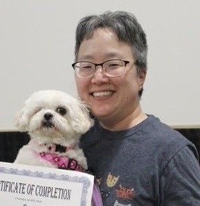 An Asian woman with gray and black hair and glasses holding a small white fuzzy dog