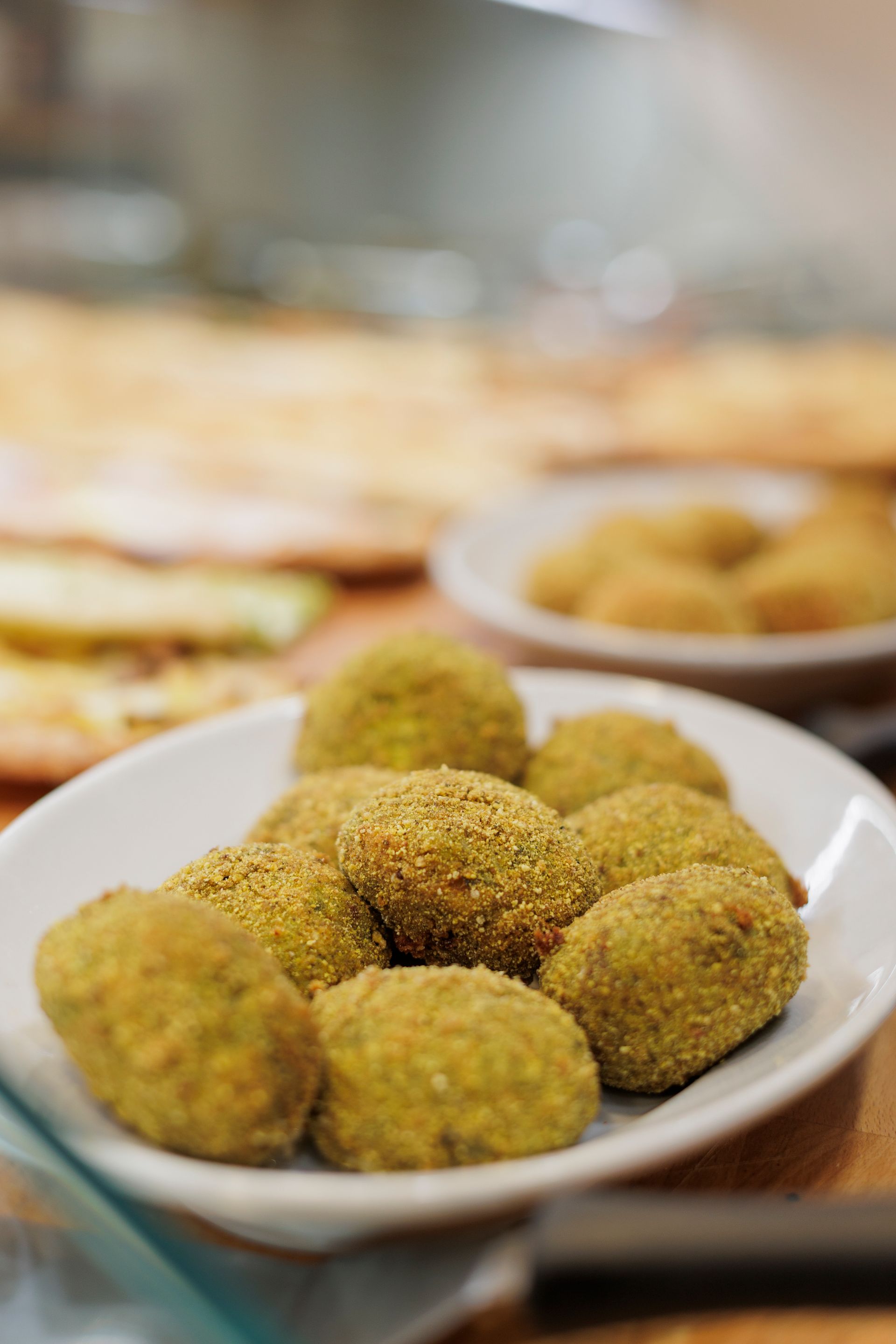 Una ciotola piena di arancini fritti dorati, con altro cibo visibile sullo sfondo sfocato.