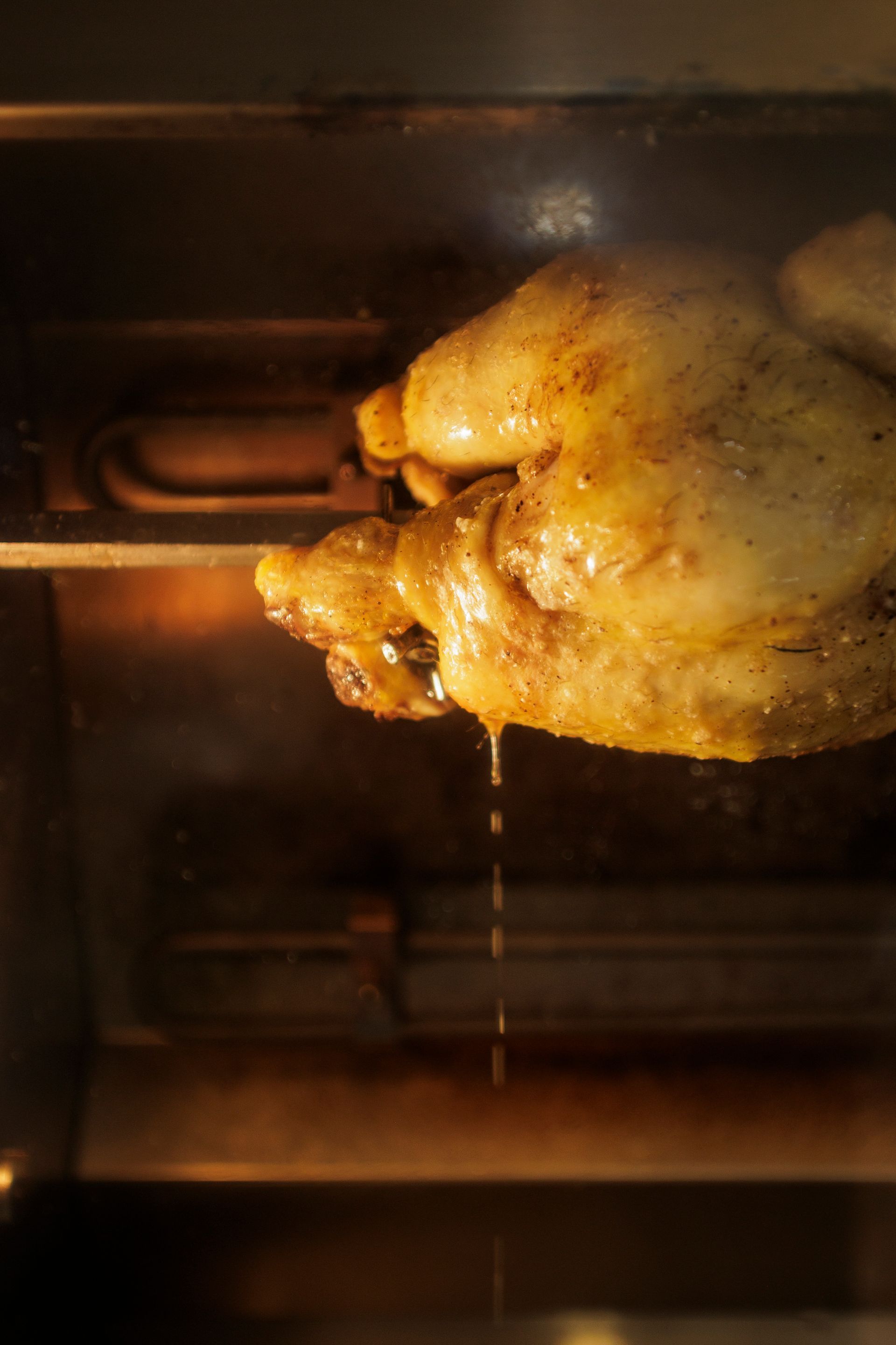 Un pollo intero arrostito su uno spiedo, con i succhi che colano dalla pelle condita all'interno di un forno acceso.