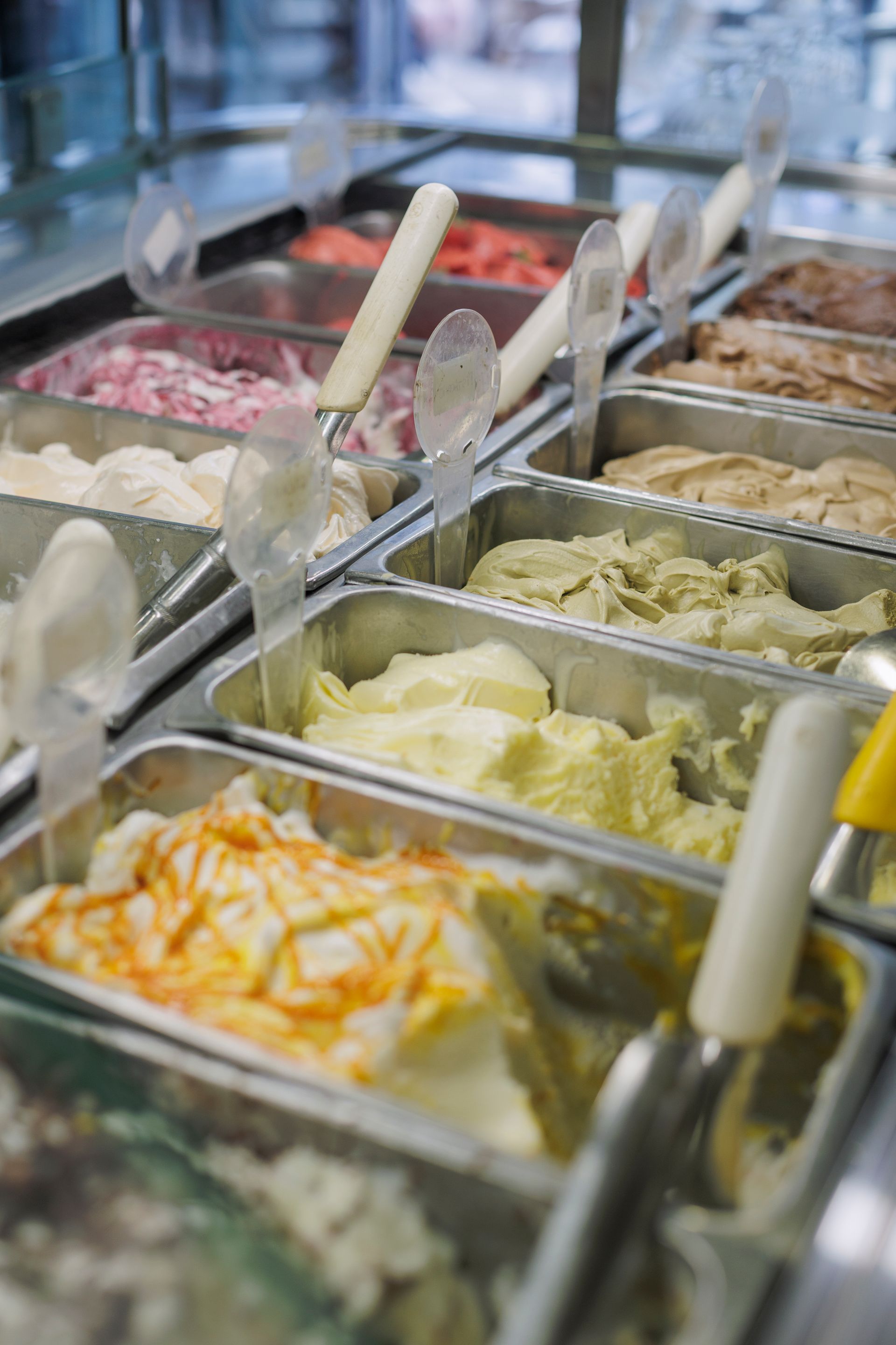 In una gelateria, una varietà di gusti di gelato esposti in vassoi di metallo all'interno di una vetrina.