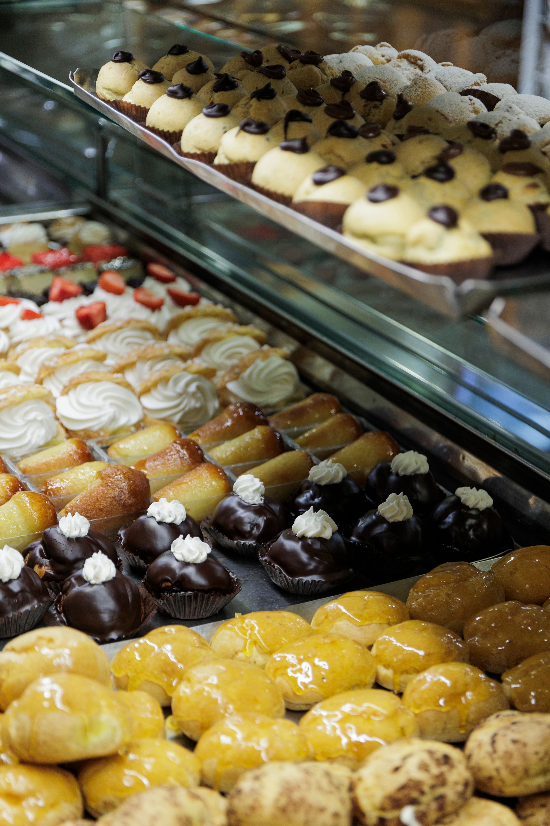 Una vetrina piena di file di pasticcini assortiti, tra cui bignè alla crema, torte glassate e dolcetti al cioccolato.