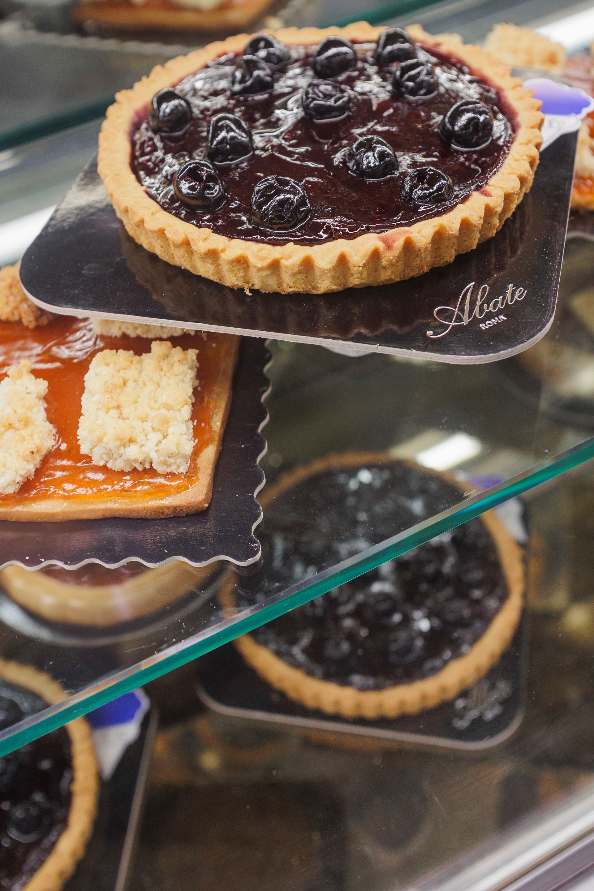 Una vetrina contenente diverse crostatine di frutta con ripieno di marmellata di mirtilli e albicocche, disposte su piccoli vassoi.