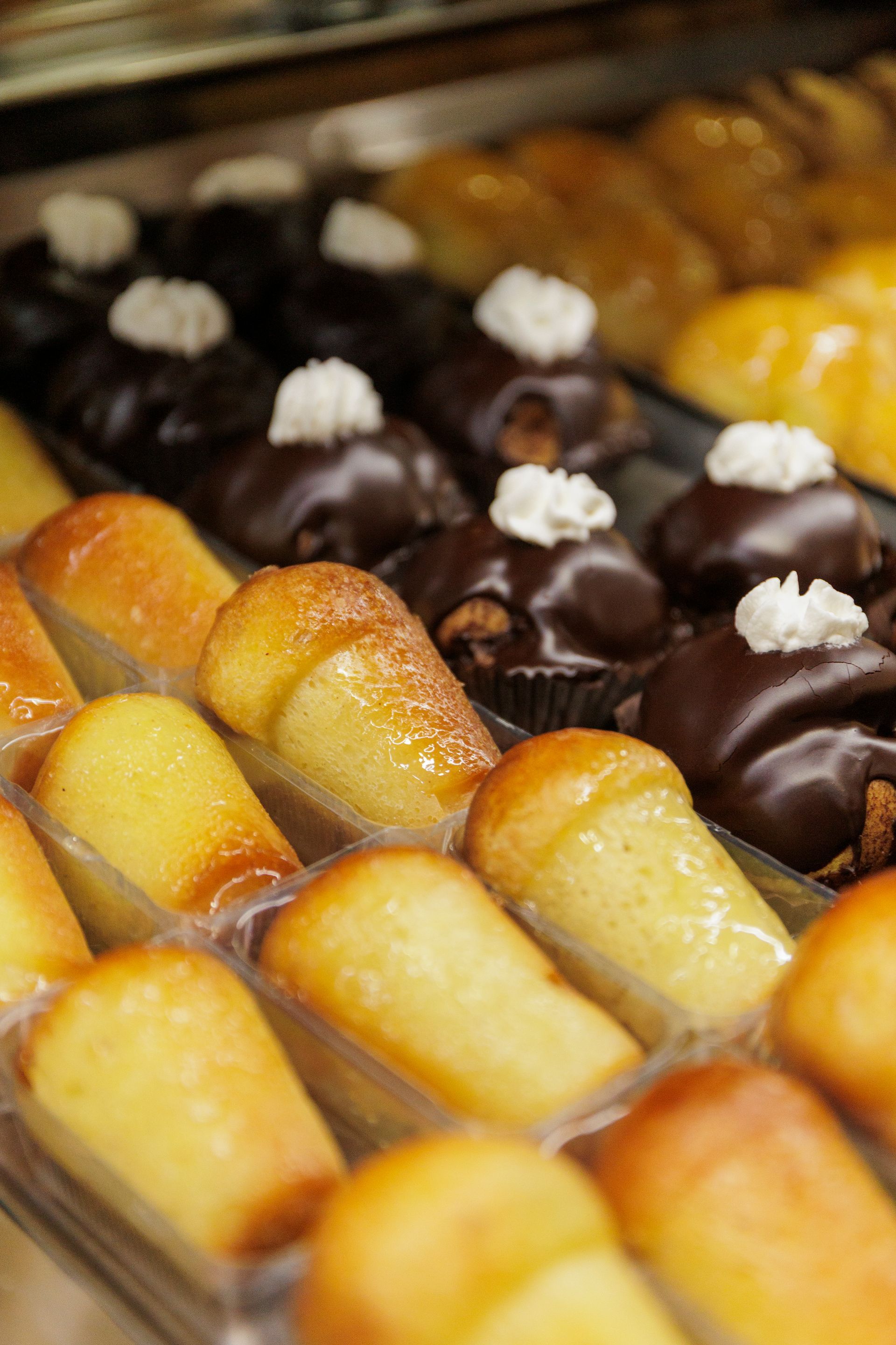 Una vetrina piena di file di babà lucidi e imbevuti di rum e pasticcini ricoperti di cioccolato e guarniti con panna.