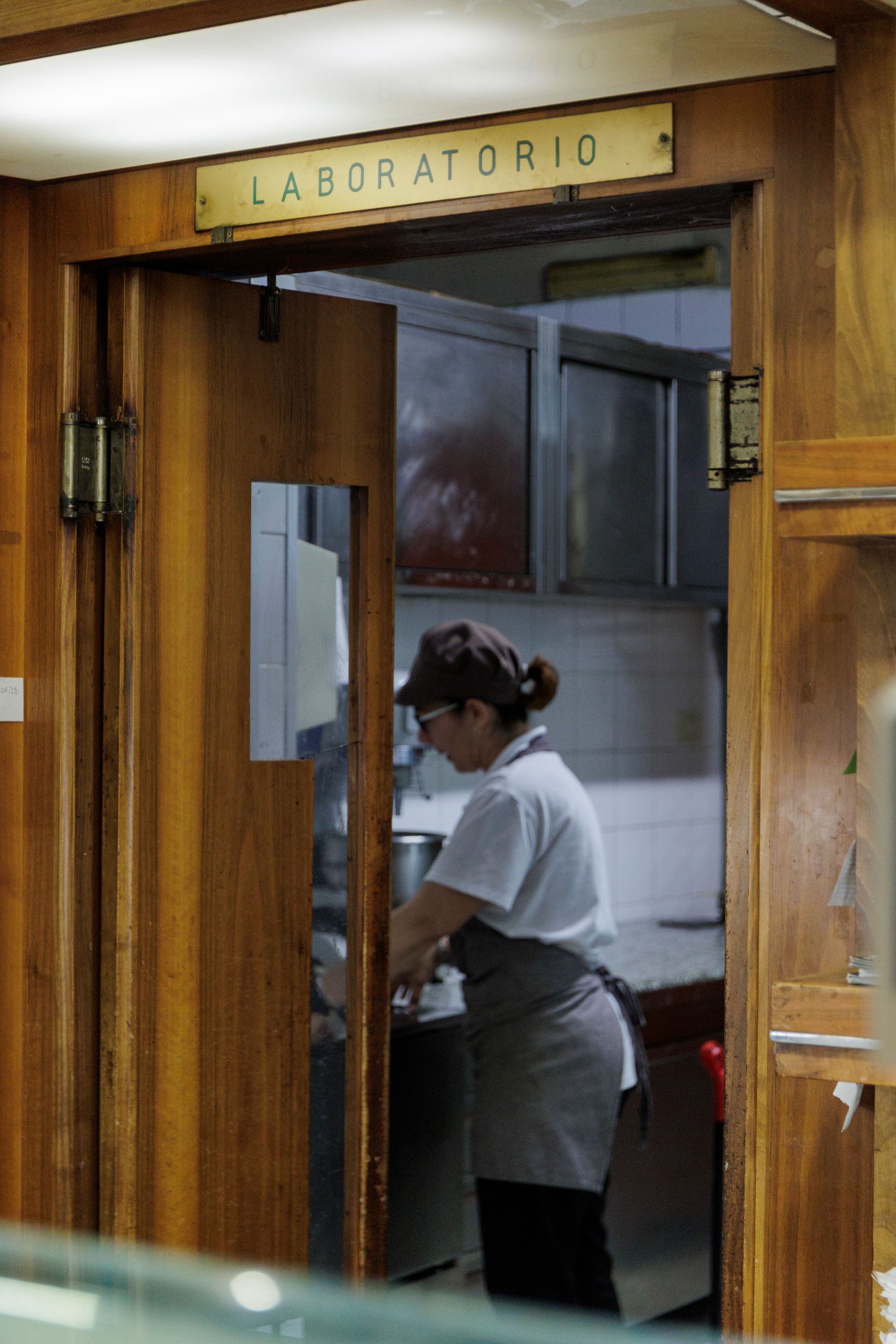 Una persona in uniforme bianca e grembiule grigio lavora in una cucina con la scritta 