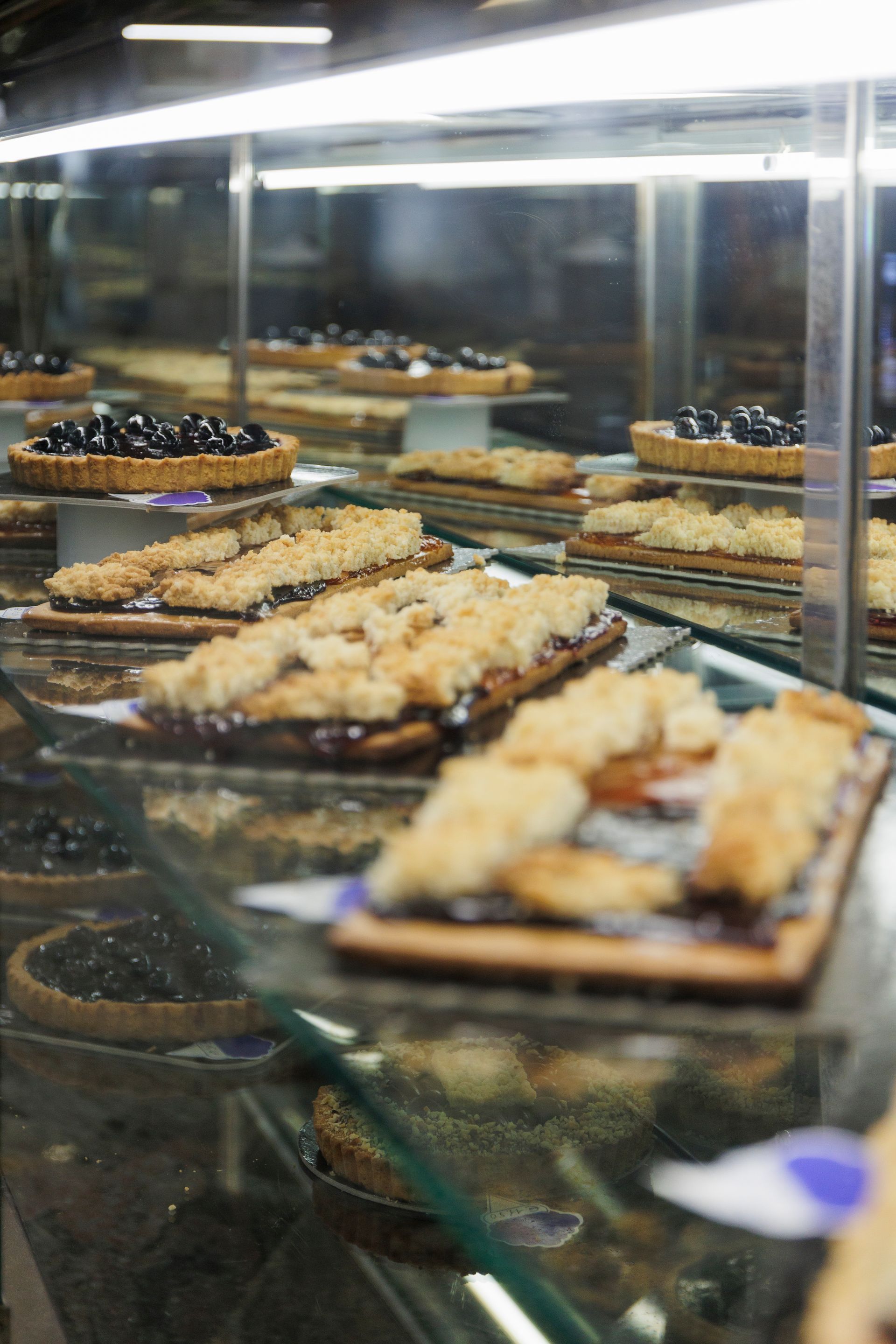 In una pasticceria, una vetrina piena di file di crostate di frutta assortite e pasticcini ricoperti di briciole.