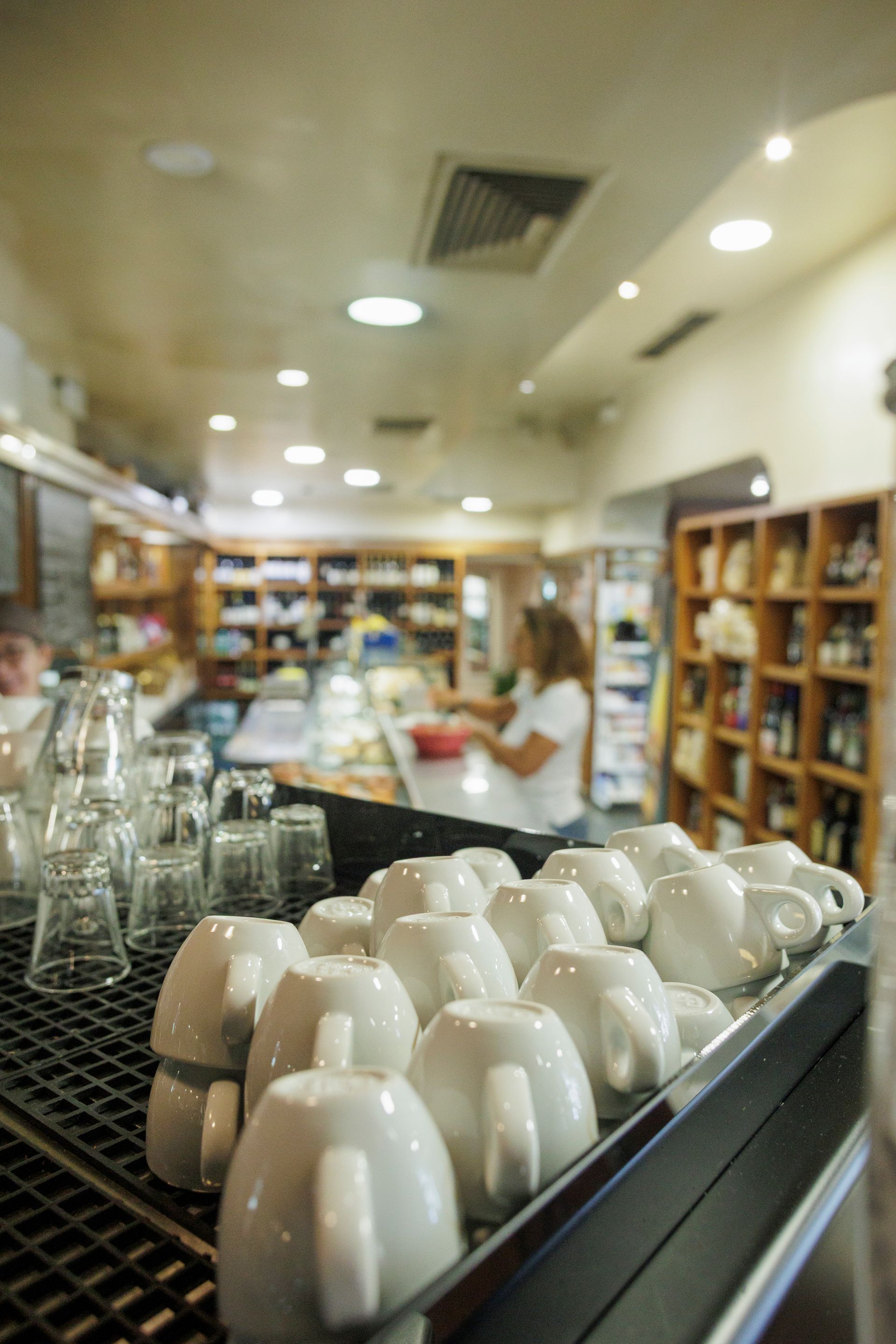 Una collezione di tazzine da caffè in ceramica bianca su un supporto nero in primo piano nell'interno di una caffetteria leggermente sfocata.
