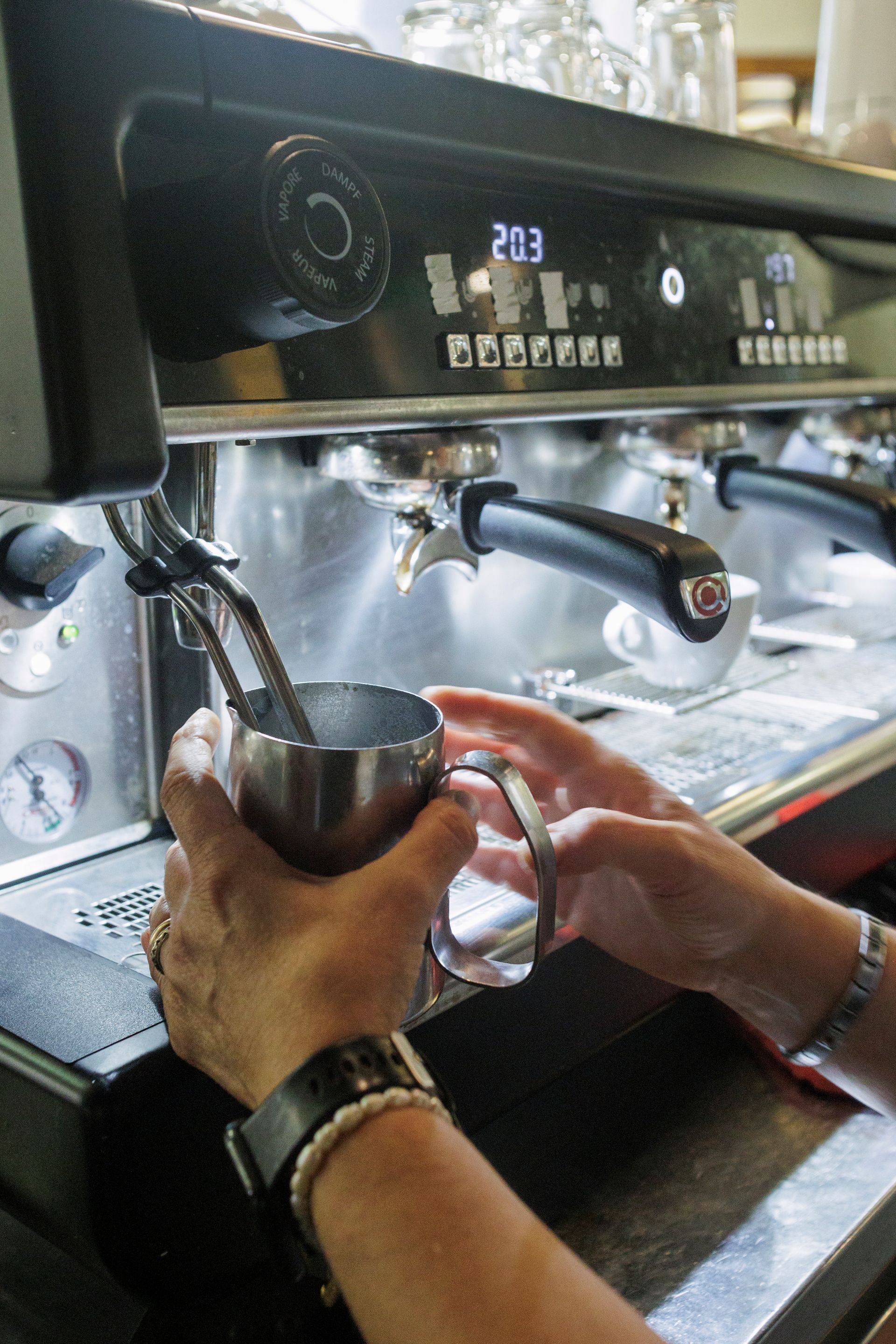 Una persona utilizza la lancia vapore di una macchina da caffè espresso professionale per montare il latte in una caraffa di metallo.