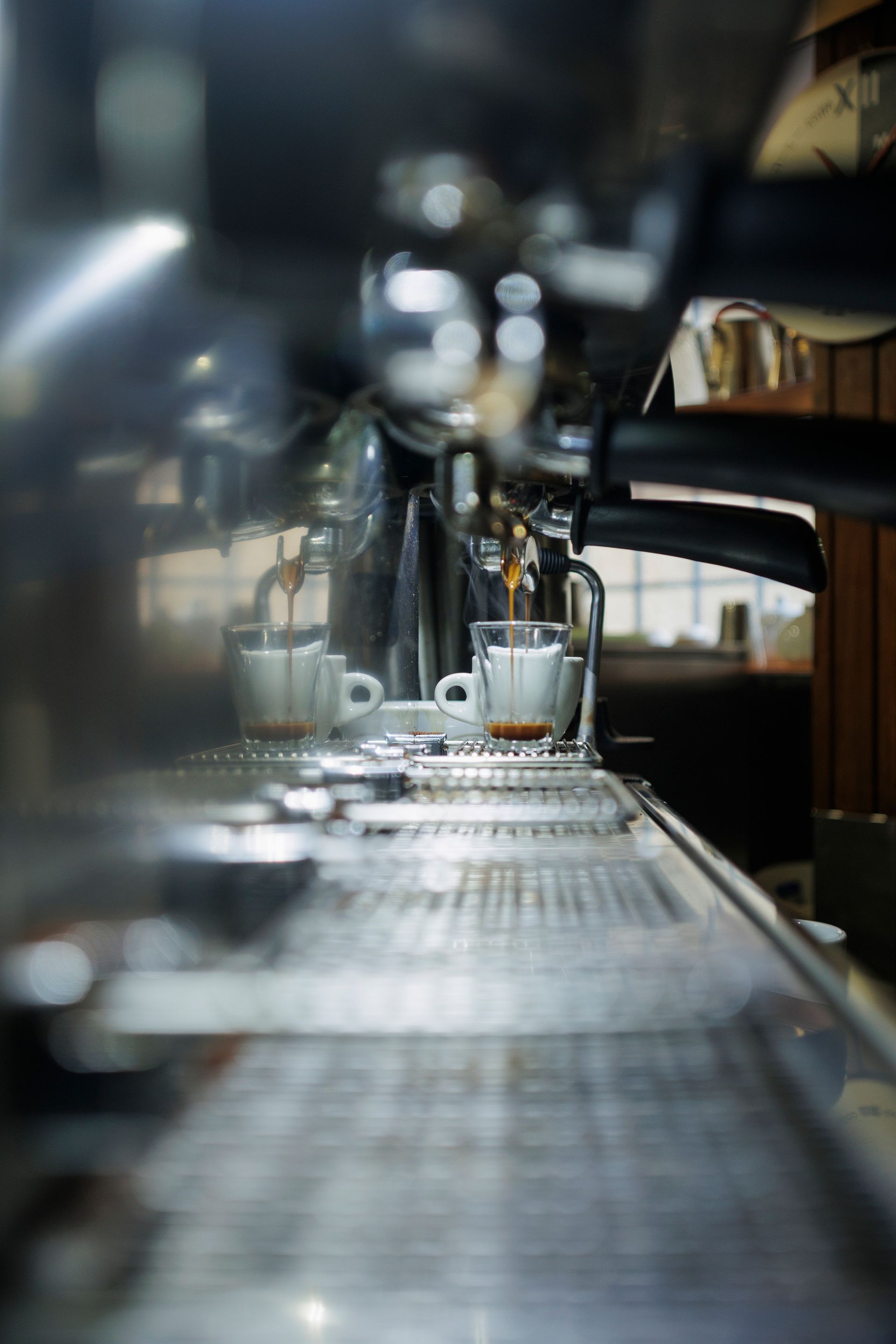 In un bar scarsamente illuminato, due tazzine da caffè espresso sono appoggiate sul vassoio di una macchina da caffè professionale e vengono riempite con dosi di espresso.