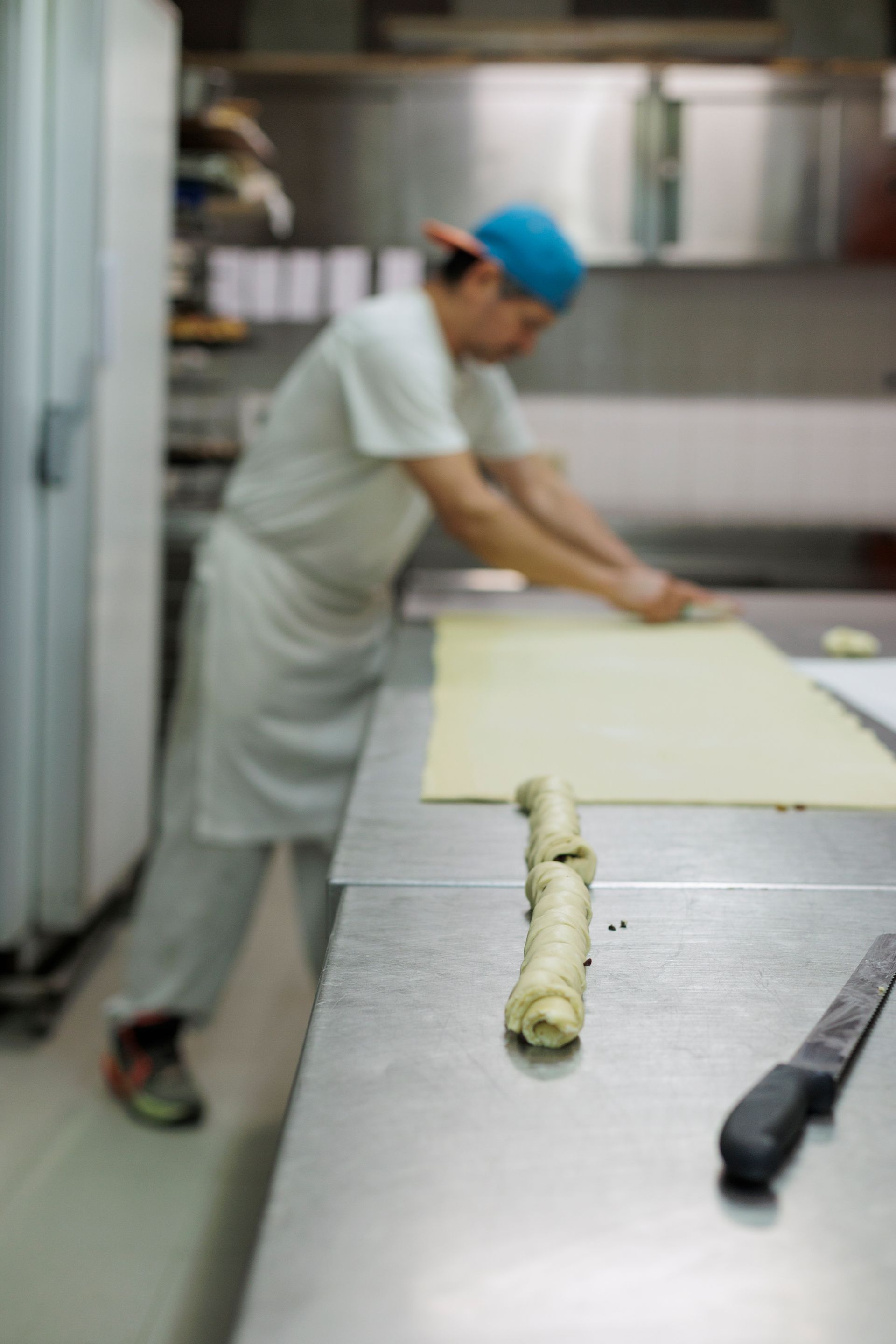 In una cucina professionale, una persona utilizza un mattarello per stendere l'impasto, con un pezzo di pasta steso sul bancone.