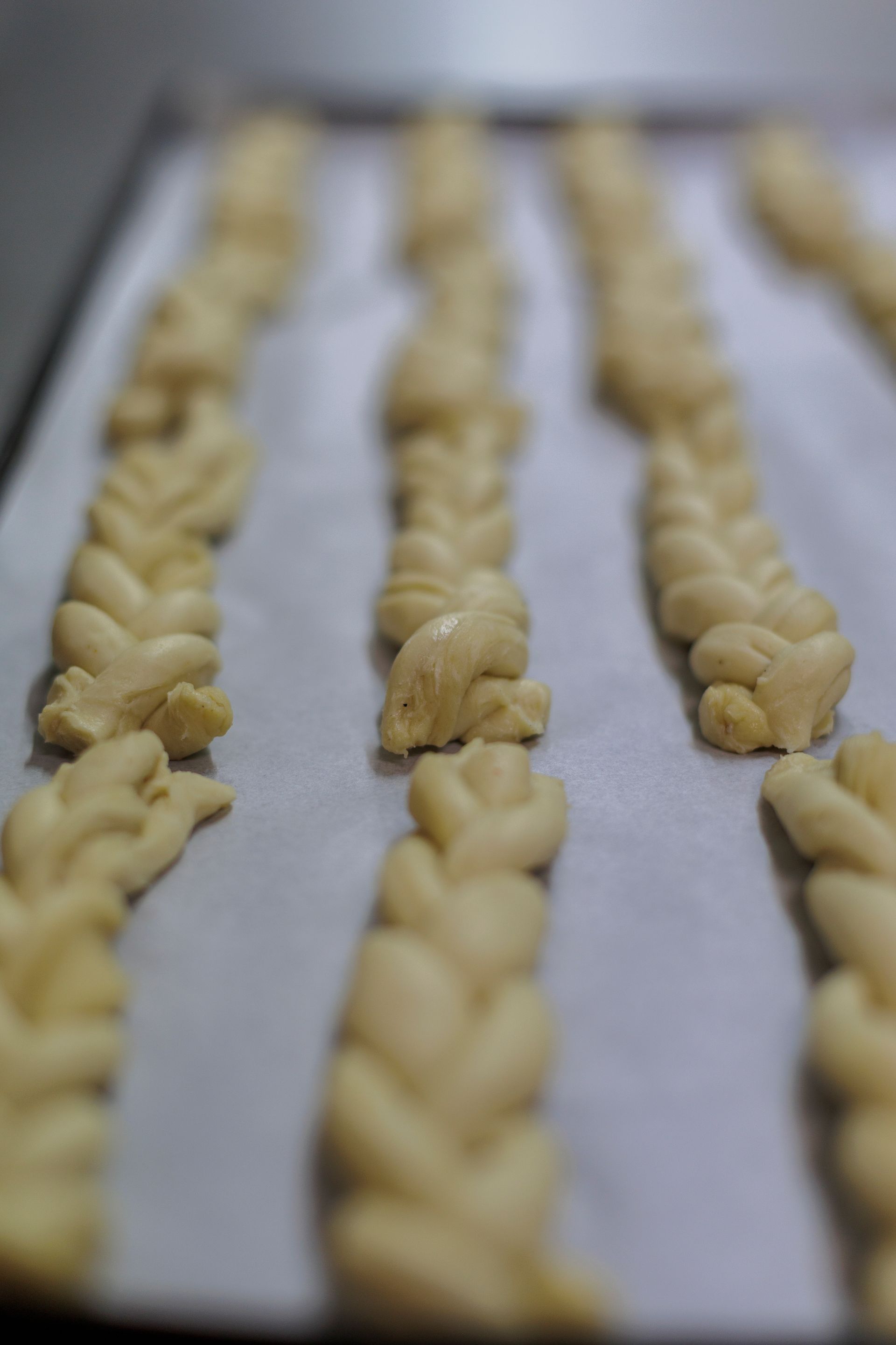 Diverse file di pezzi di pasta intrecciata disposte su una teglia bianca rivestita di carta da forno.