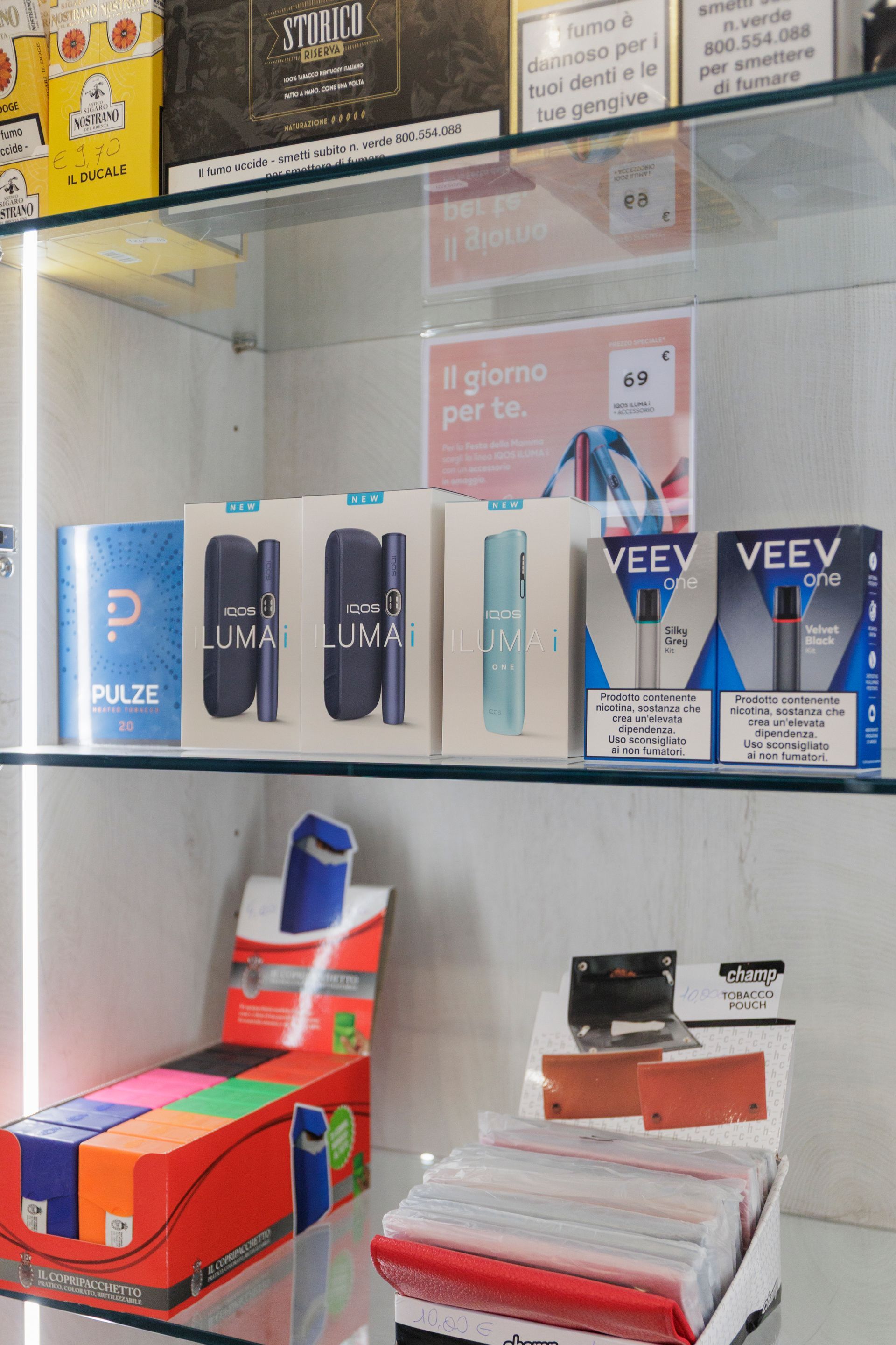 Su uno scaffale di un negozio sono esposti vari dispositivi per sigarette elettroniche Veev e Pulze e accessori per lo svapo, confezionati in scatole.