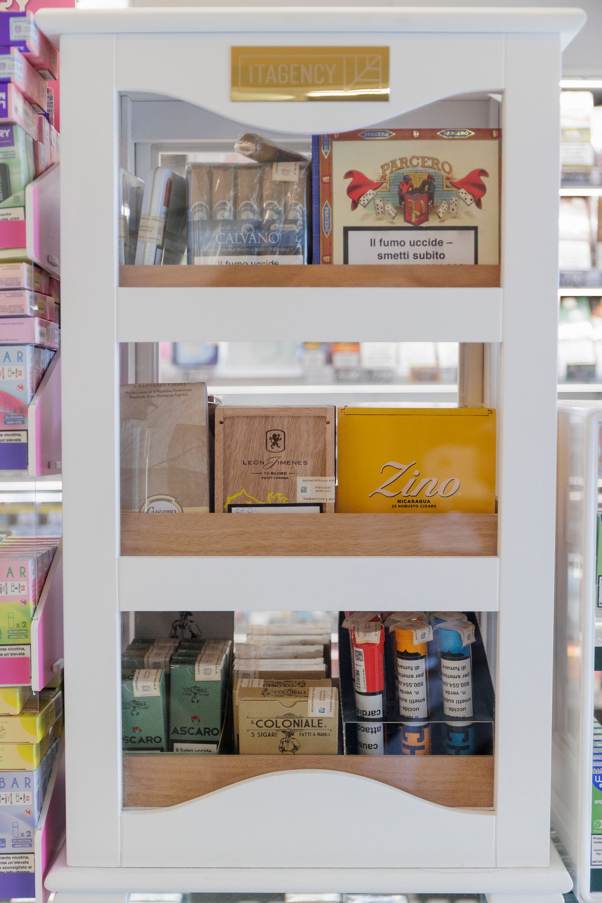 Una vetrina bianca a tre ripiani contenente varie scatole di sigari e prodotti del tabacco.