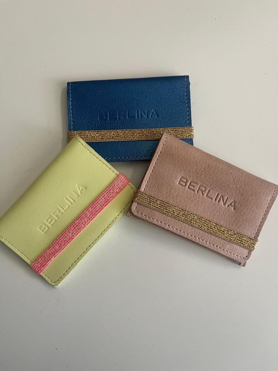 Tres pequeños tarjeteros rectangulares de la marca Berlina en azul, amarillo y rosa, cada uno acentuado
