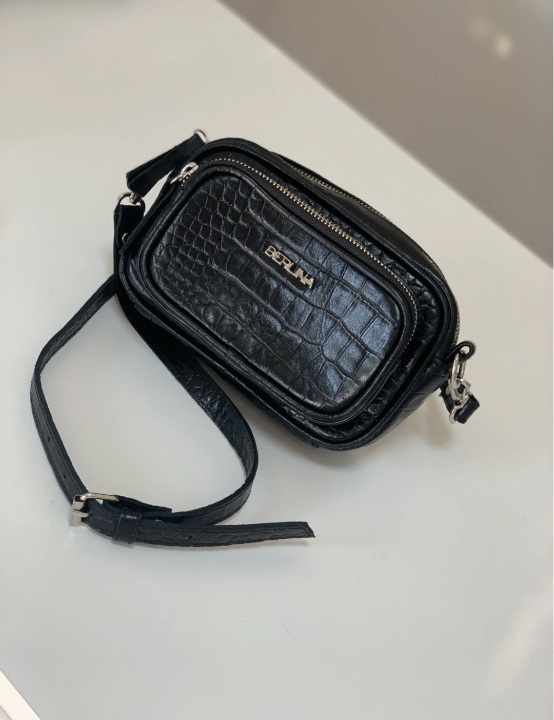 Un pequeño bolso bandolera negro con textura de cocodrilo