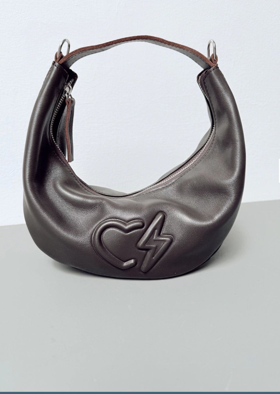Un bolso de mano de cuero de color marrón oscuro en forma de media luna con un corazón en relieve