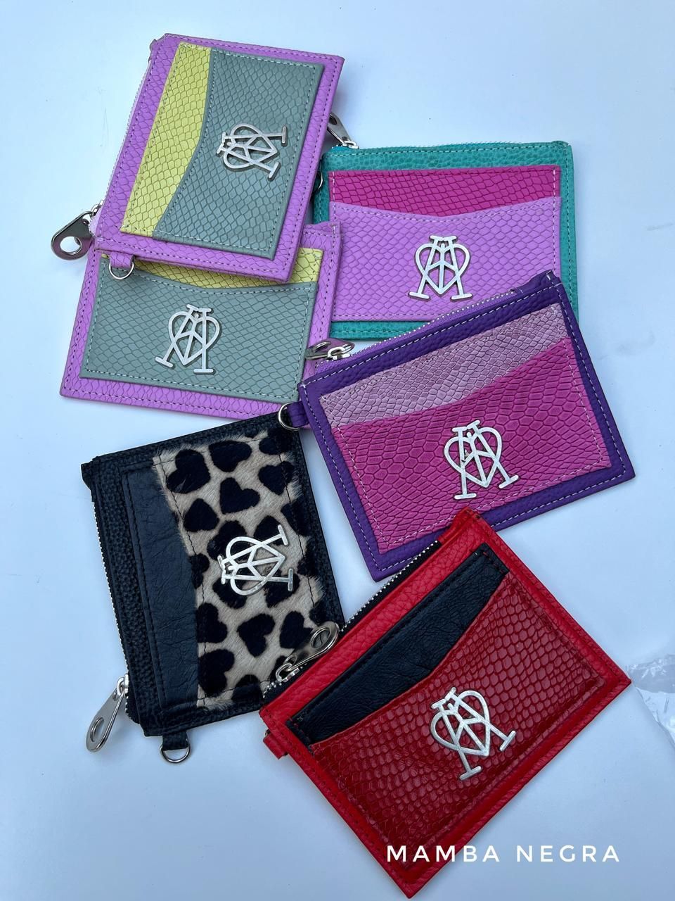 Cinco pequeñas carteras para tarjetas en varios colores y texturas, cada una con un logotipo de metal centrado