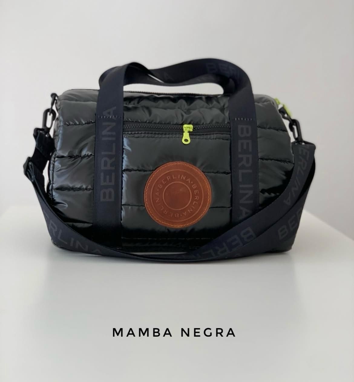 Un bolso cilíndrico acolchado de color negro con correas con la marca 