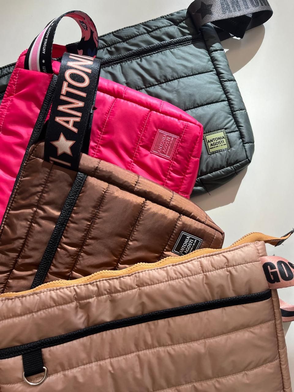 Una pila de cuatro bolsos acolchados con cierre de cremallera en verde oscuro, rosa brillante,