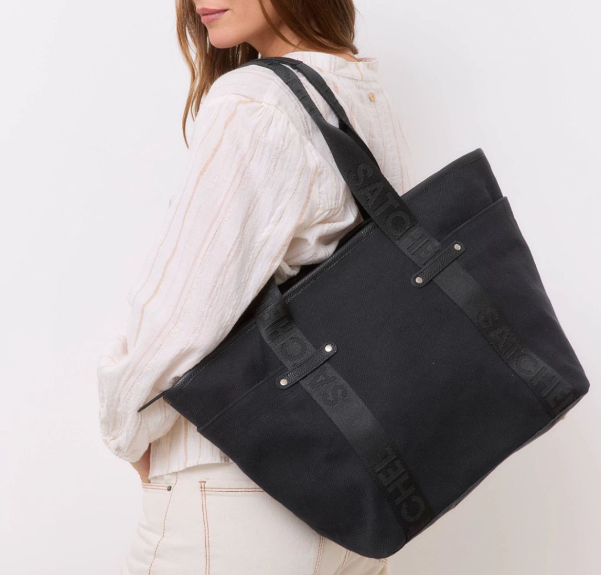 Una persona que viste una camisa blanca lleva una bolsa de lona negra sobre su hombro sobre un fondo blanco liso.
