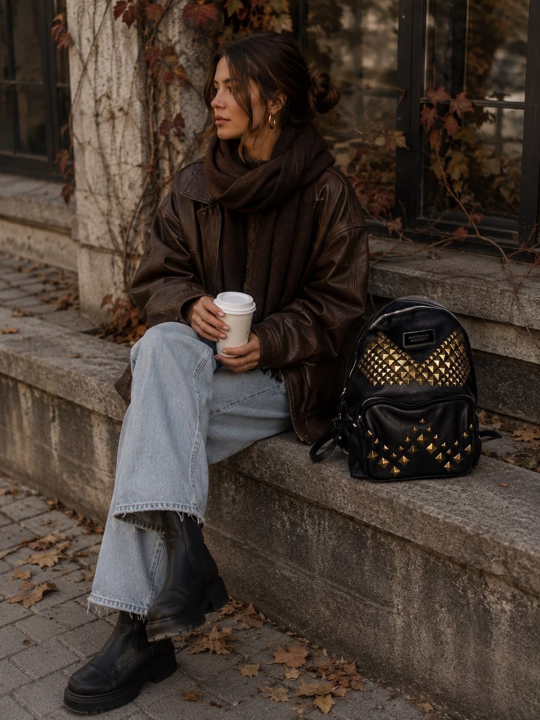 Una persona viste un cárdigan colorido con estampado en zigzag y lleva una mini mochila negra con tachuelas al aire libre.