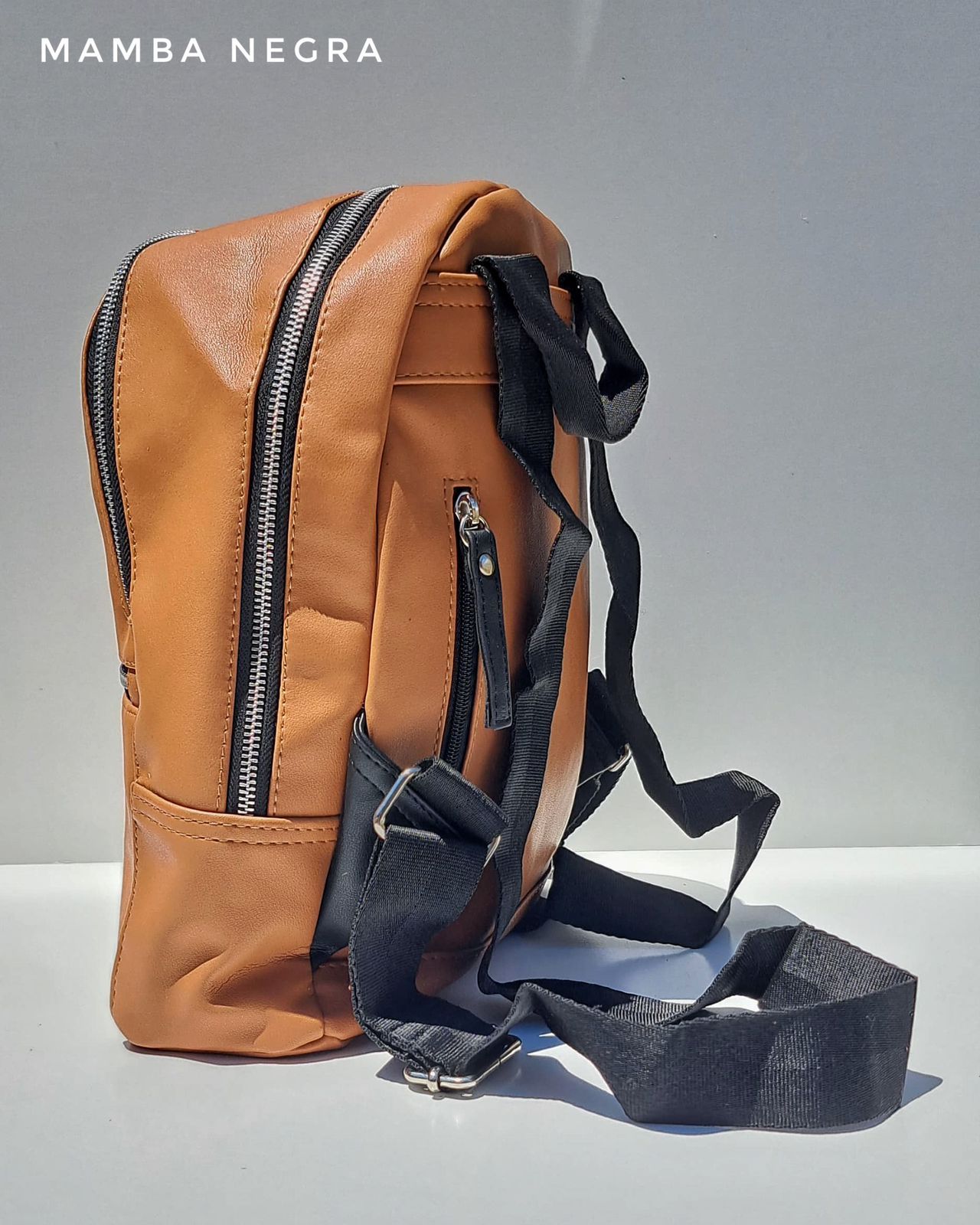 Mochila minimalista de color tostado con cremalleras negras y correas ajustables negras sobre un fondo blanco.