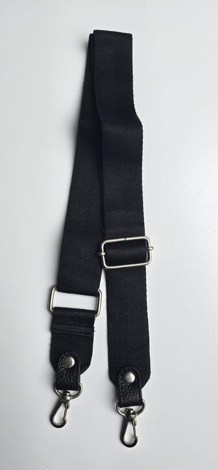 Una correa de hombro de nailon ajustable de color negro con herrajes metálicos en tono plateado