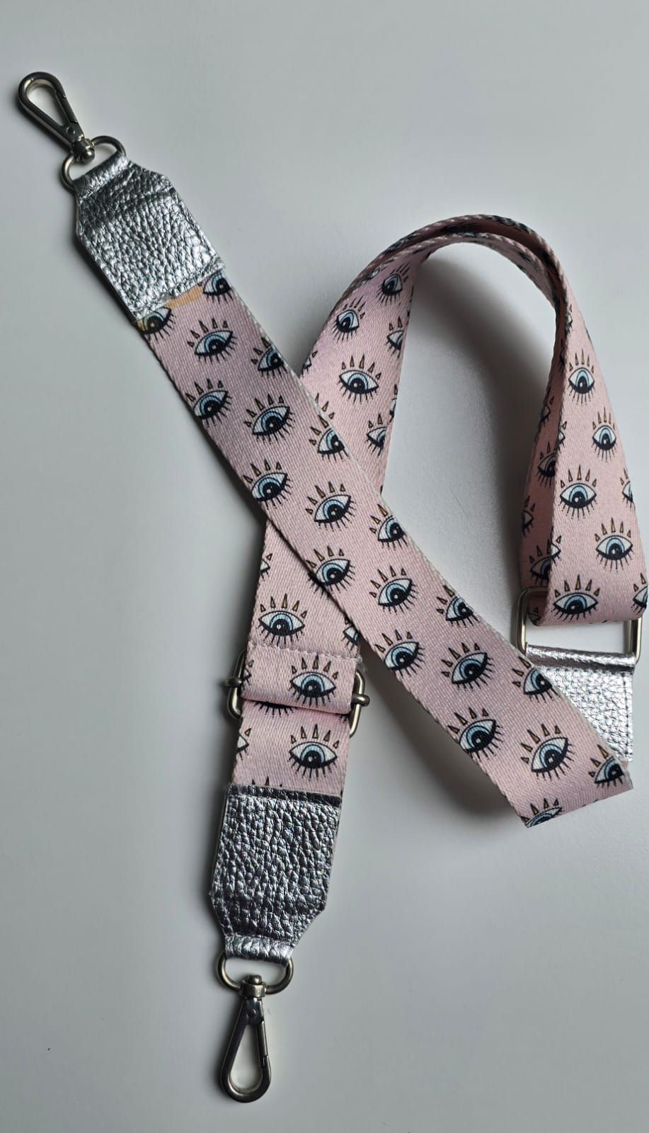 Una correa de bolso rosa con un patrón de ojos negros, herrajes plateados