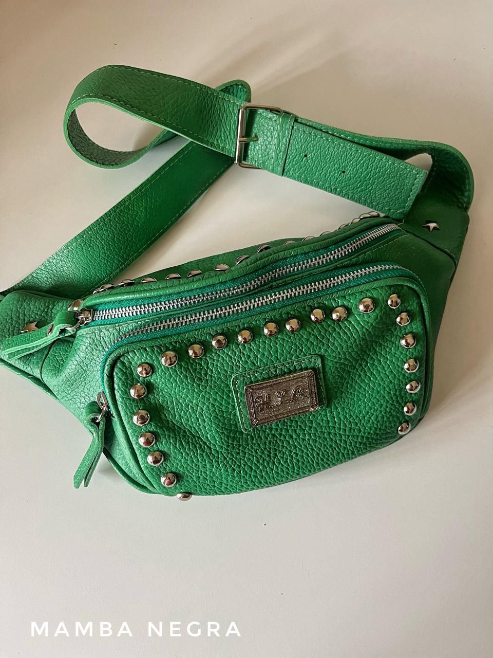 Un bolso con cinturón de piel texturizada de color verde vibrante que presenta detalles de tachuelas plateadas