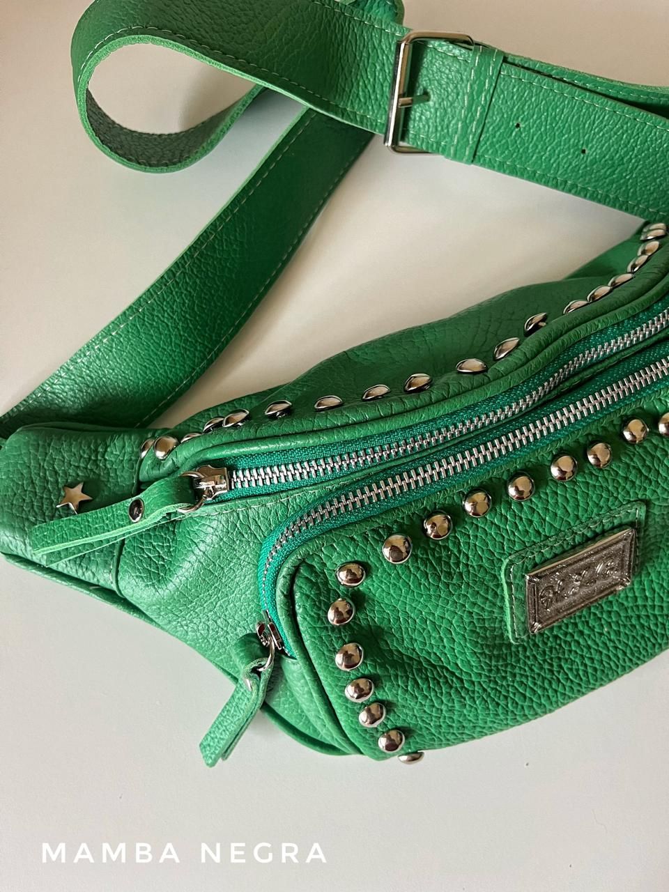 Un bolso con cinturón de piel texturizada de color verde vibrante que presenta detalles de tachuelas plateadas