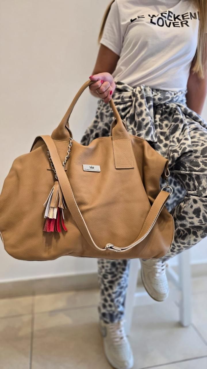 Una persona sostiene un bolso grande de color canela, estilo vagabundo, con un dije de borla,