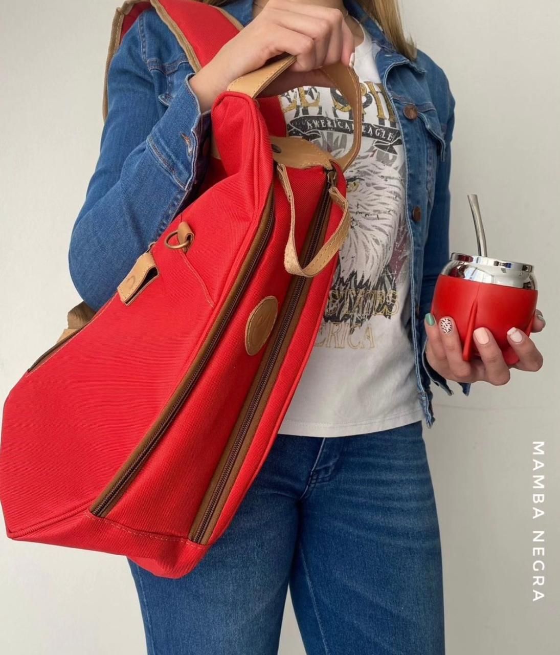 Una persona con una chaqueta de mezclilla sostiene una bolsa roja y un mate rojo a juego con una pajita de metal.