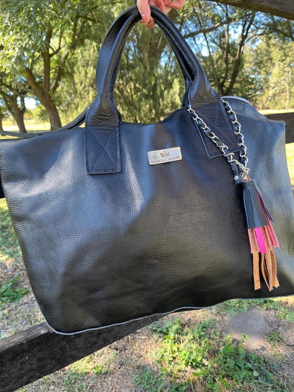 Un bolso de mano de cuero negro texturizado con un dije de cadena con flecos rosas